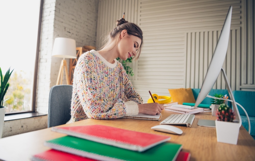 young woman studying at home office desk with computer in cozy and comfortable interior during daylight